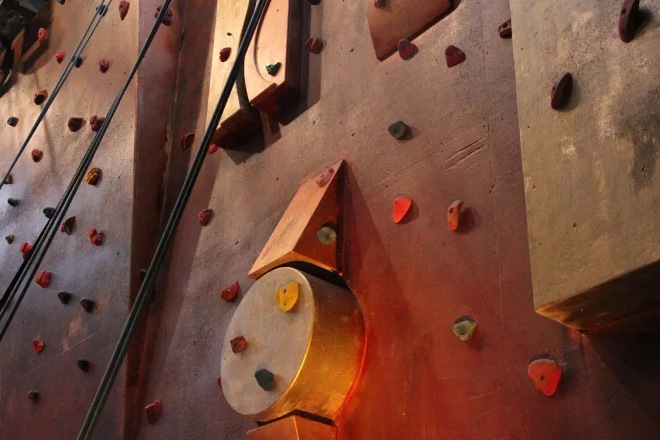 Top ropes hanging beside wooden volumes and coloured holds on the climbing wall
