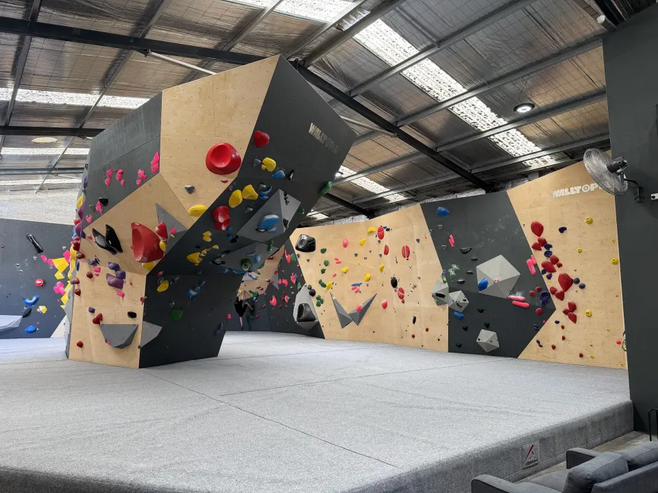 Angled plywood and grey bouldering walls above deep grey matting