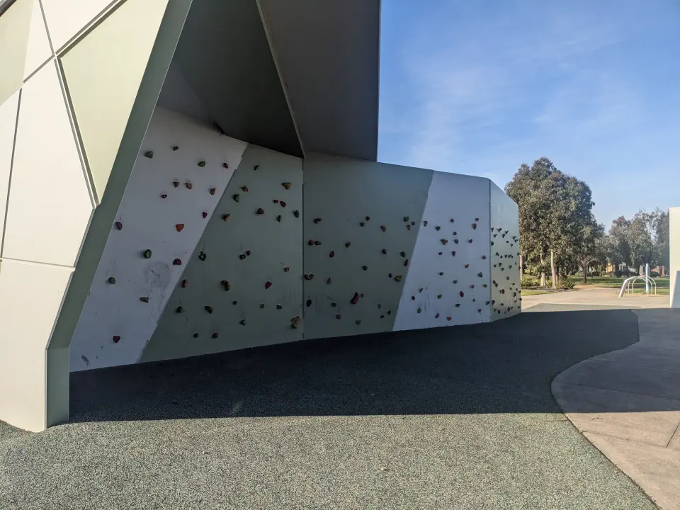 Angled bouldering panels under a canopy, with rubber safety surfacing in front