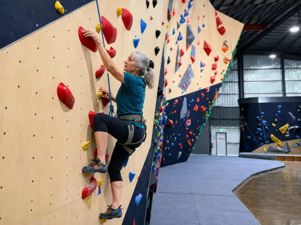 Climber on a roped route along the long timber wall, with the bouldering area behind