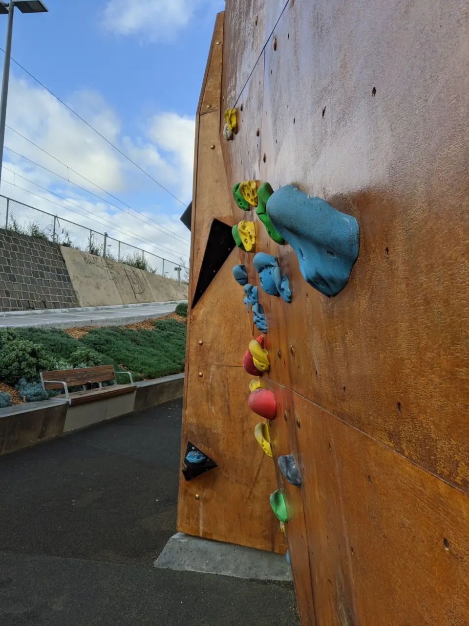 The end of the wall with a line of holds and a blue volume, beside the trail