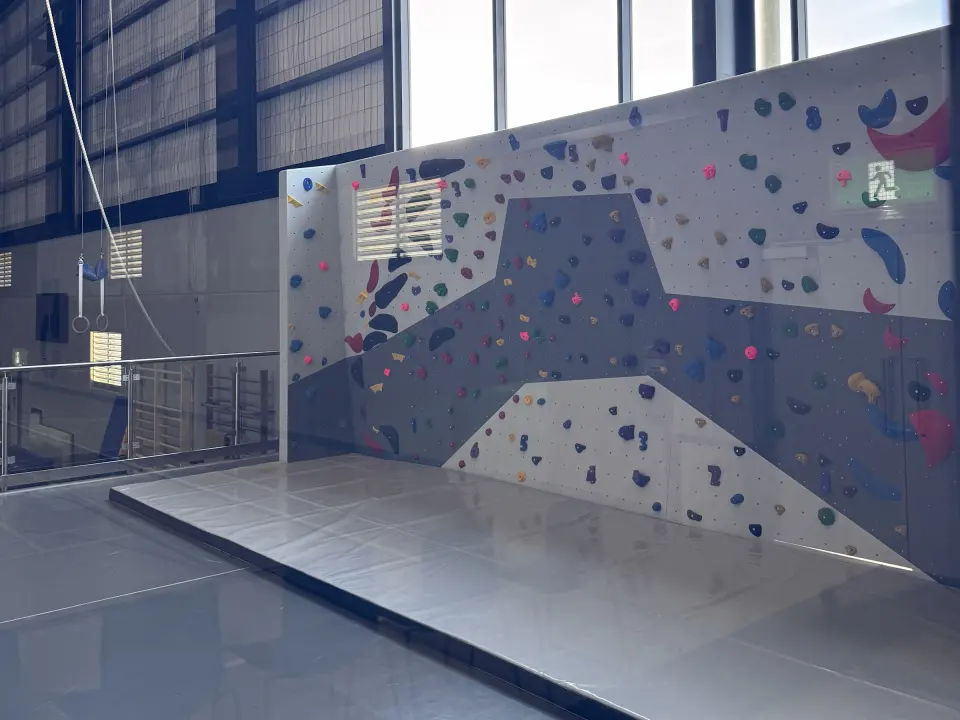 Grey and white climbing wall above thick matting, with tall windows behind