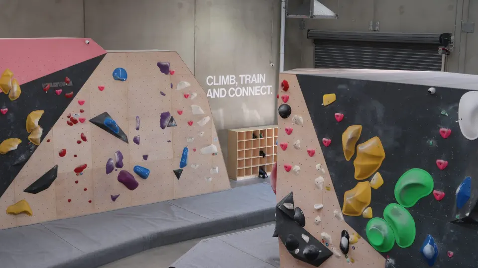 Pink, black and timber bouldering walls with coloured holds above deep matting