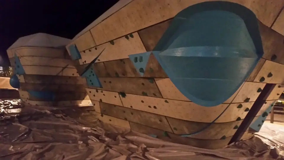 The bouldering wall's curved blocks and blue volumes at night