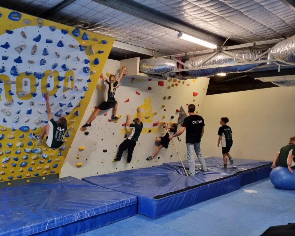 Bouldering wall with a yellow panel above blue crash mats