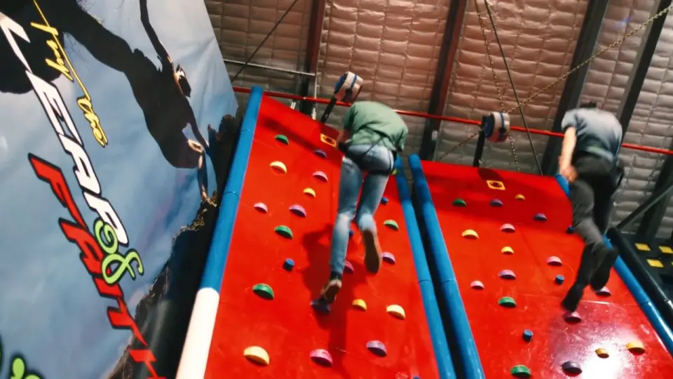 Two climbers racing up the red walls beside the Leap of Faith banner