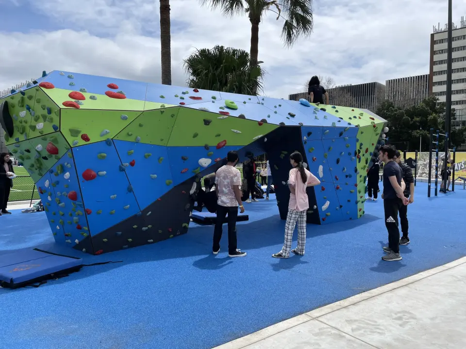 Blue and green faceted bouldering wall on blue rubber flooring, with students gathered around it