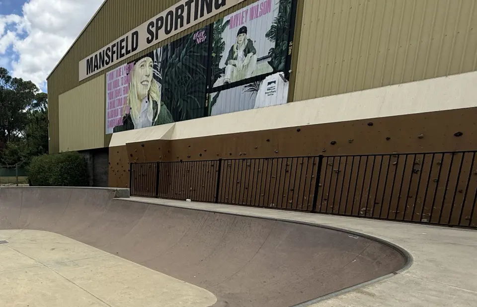 Bouldering wall along the base of the Mansfield Sporting Complex, fenced off from the skate bowl, below a mural