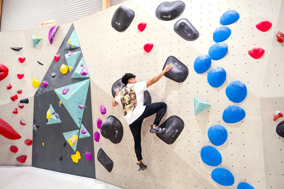 A climber bouldering on a wall of blue, black and red holds at BlocHaus Fyshwick, Canberra