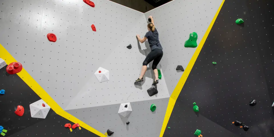 A climber on a grey wall between black panels at Industry Boulders, a bouldering gym in Grovedale, Geelong