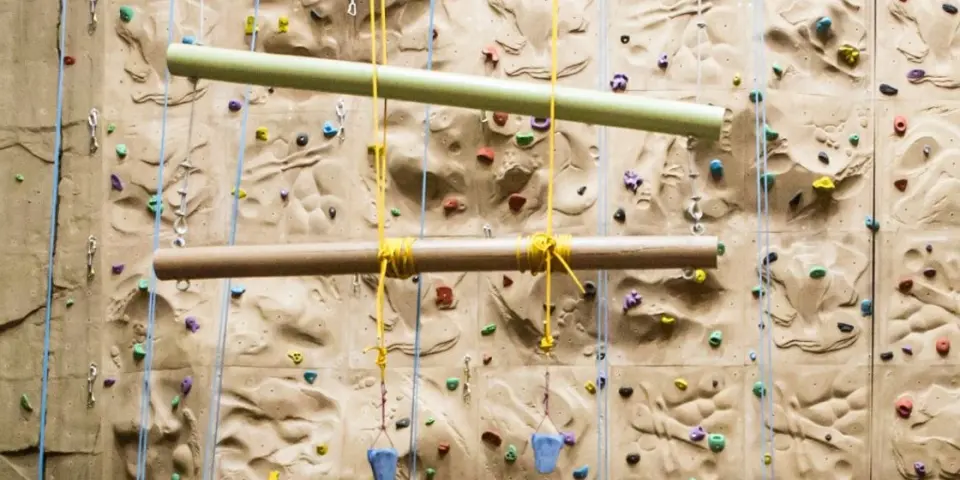 Coloured holds and top ropes on the textured wall, with two suspended logs