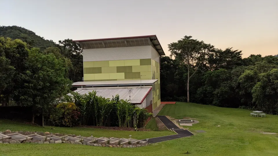 Side of the climbing hall and its lower annex, set on a lawn at the rainforest's edge