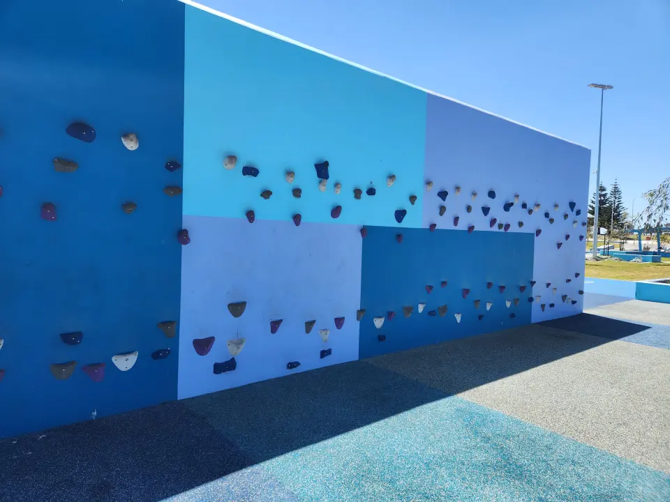 Blue climbing wall with coloured bolt-on holds above a rubber soft-fall surface