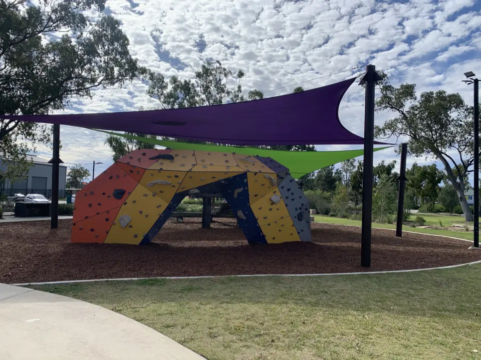 Orange, yellow, navy and grey bouldering arch on bark softfall under purple and green shade sails