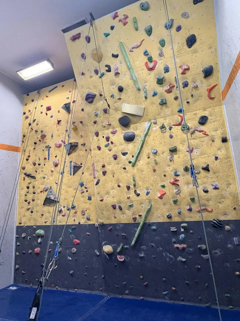 Top ropes hanging down the yellow wall above the dark bouldering cave