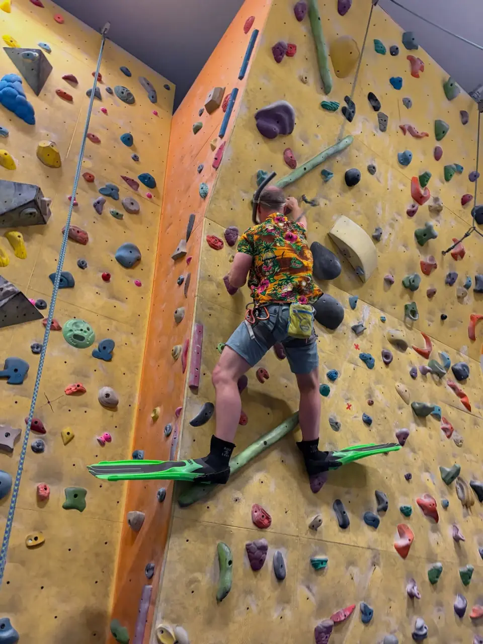 Climber in swim fins on the yellow wall at the club's fun dress climbing night