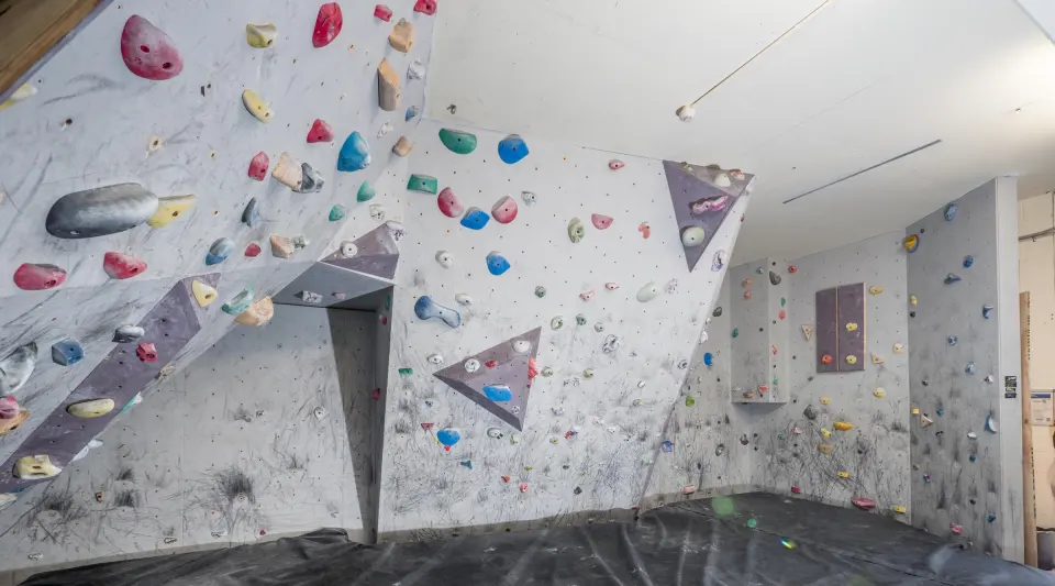 Grey bouldering walls with angled panels and coloured holds above black crash matting