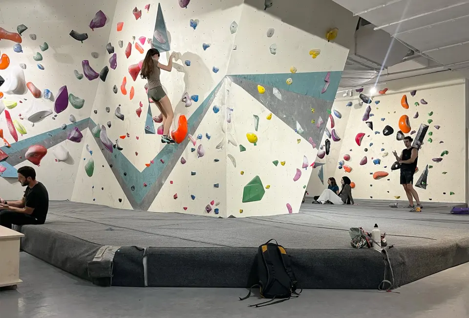 Climber on a wall with large volumes above thick matting